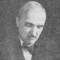 Edward Kuntze. Łysiejący meżczyzna  w średnim wieku pochyla się nad czymś. Ubrany w marynarkę i muchę.