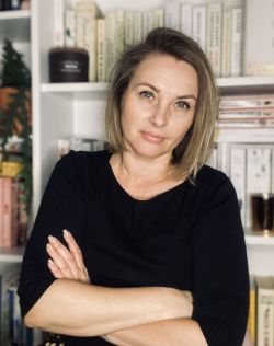 Elżbieta Staroń, uśmiechnięta kobieta w blond włosach do ramion, ze skrzyżowanymi rękoma patrzy w obiektyw