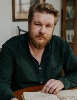 zdjęcie młodego mężczyzny w brodzie, oparty o stół z otwartą książką