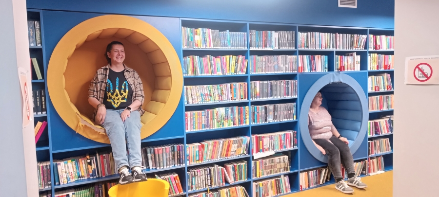 Dwie bibliotekarki siedzą w okrągłych siedziskach wbudowanych w biblioteczny regał