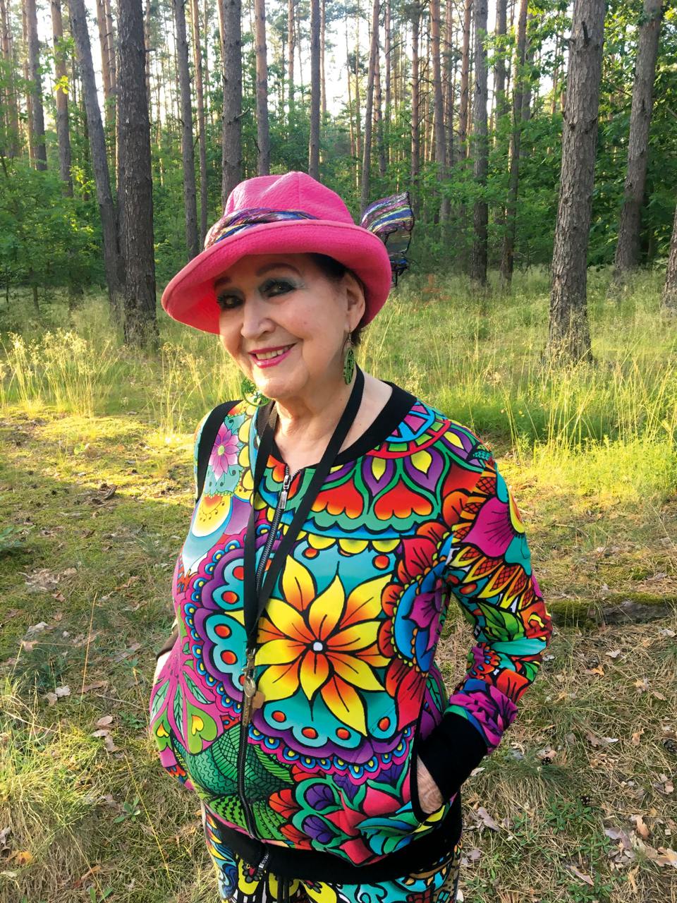 Barbara Rybałtowska, brunetka w kolorowym pstrokatym stroju i kapeluszu uśmiech się