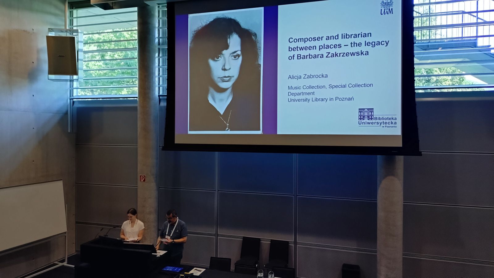 Sala wykładowa. Dwie osoby prezentują referat. Za nimi ekran ze zdjęciem Barbary Zakrzewskiej